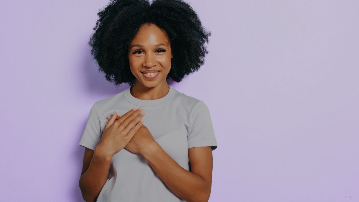 woman in grey shirt smiling with both hands on her chest (MODEL)